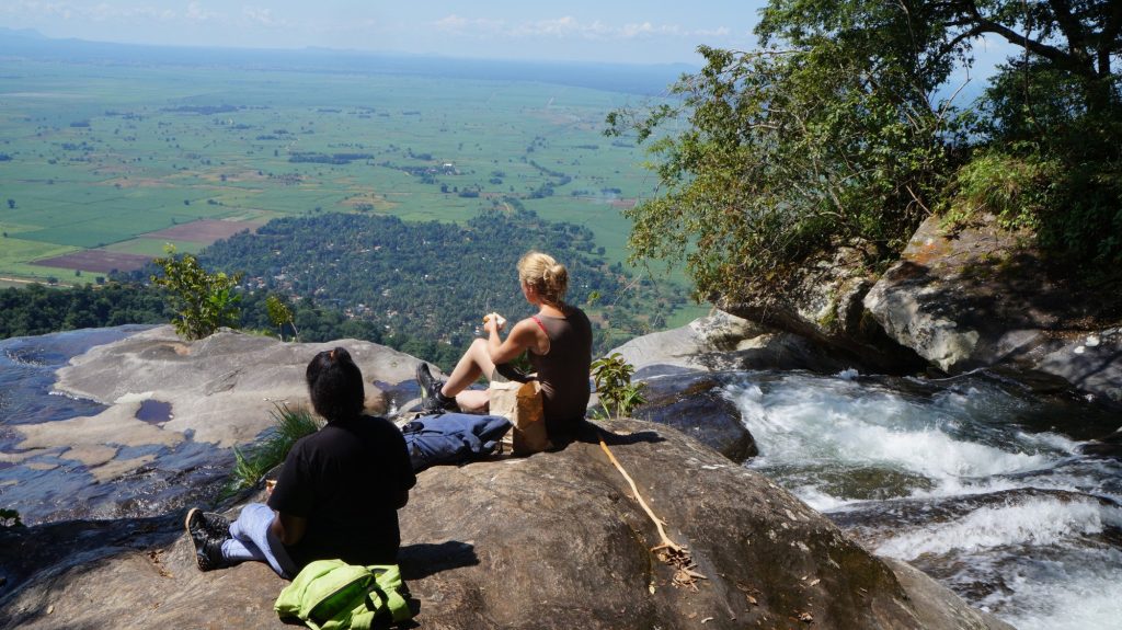 Two hikers eating lunch beside a clifftop cascade, Udzungwa Mountains National Park