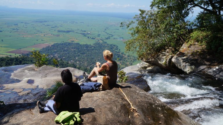 Two hikers eating lunch beside a clifftop cascade, Udzungwa Mountains National Park