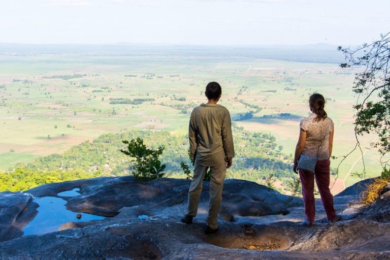 Two hikers on a rock viewpoint above the farmland plains, Udzungwa Mountains National Park