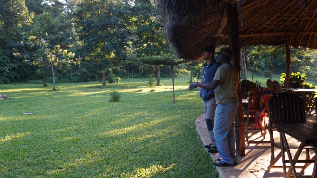 Two men on the edge of a thatched deck overlooking the lawn, Udzungwa Mountains National Park